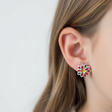 Load image into Gallery viewer, A pair of silver-toned flower-shaped earrings with red and green enamel petals and a yellow centre, shown on a clear background.